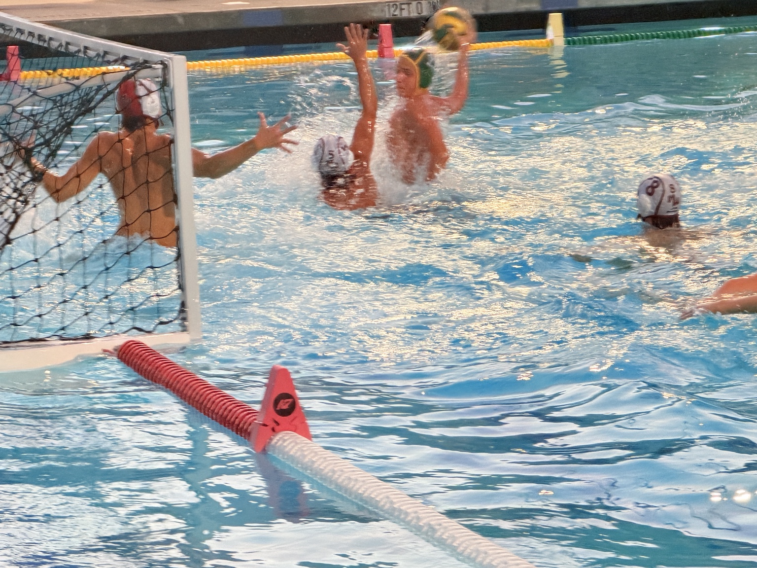 A Kingsburg attacker raises the ball as Whitney defends beside the goal.